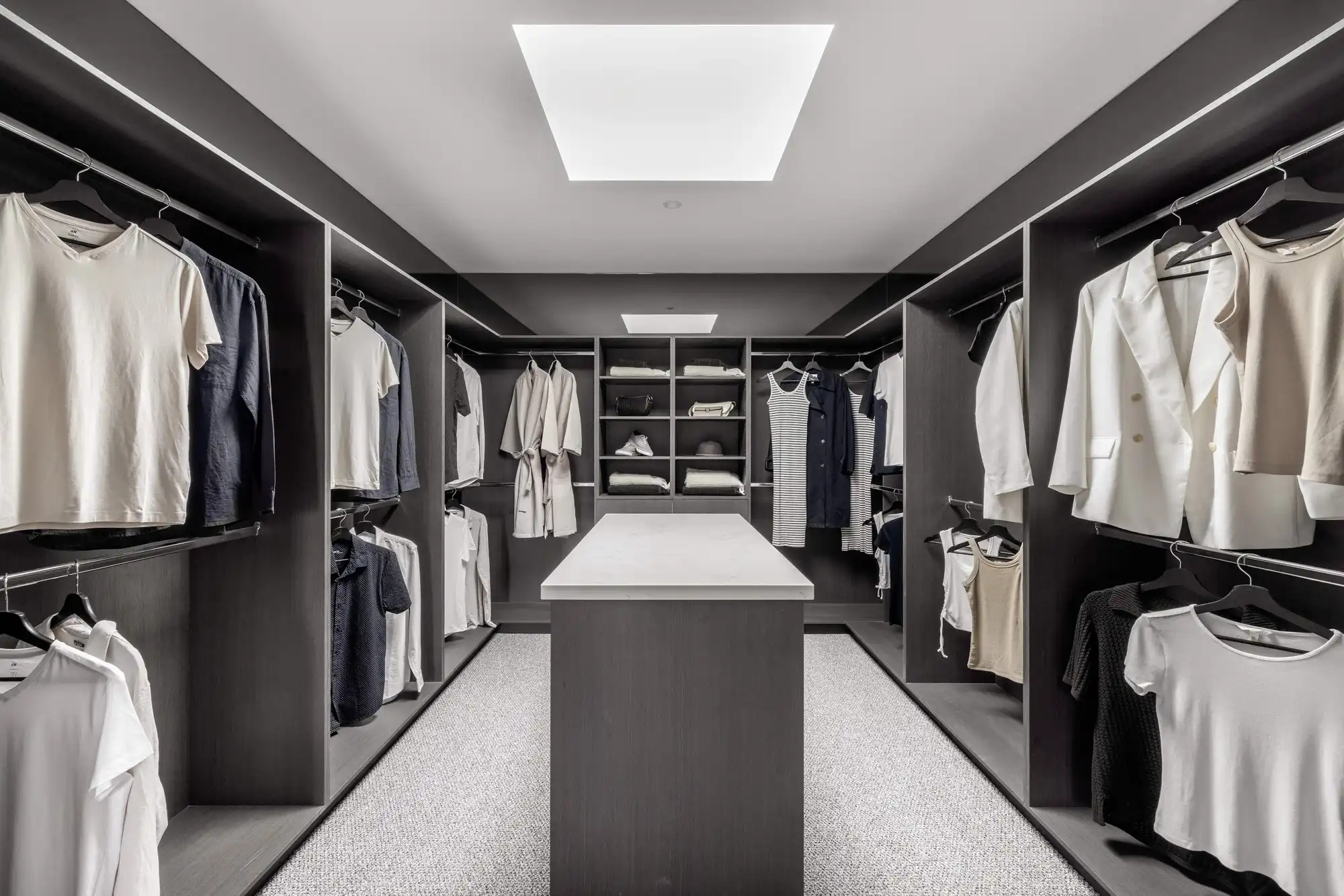 Walk-in robe at the Durrant Masterpiece home, featuring a skylight to open up the space and island benchtop in the middle for accessories to be stored.