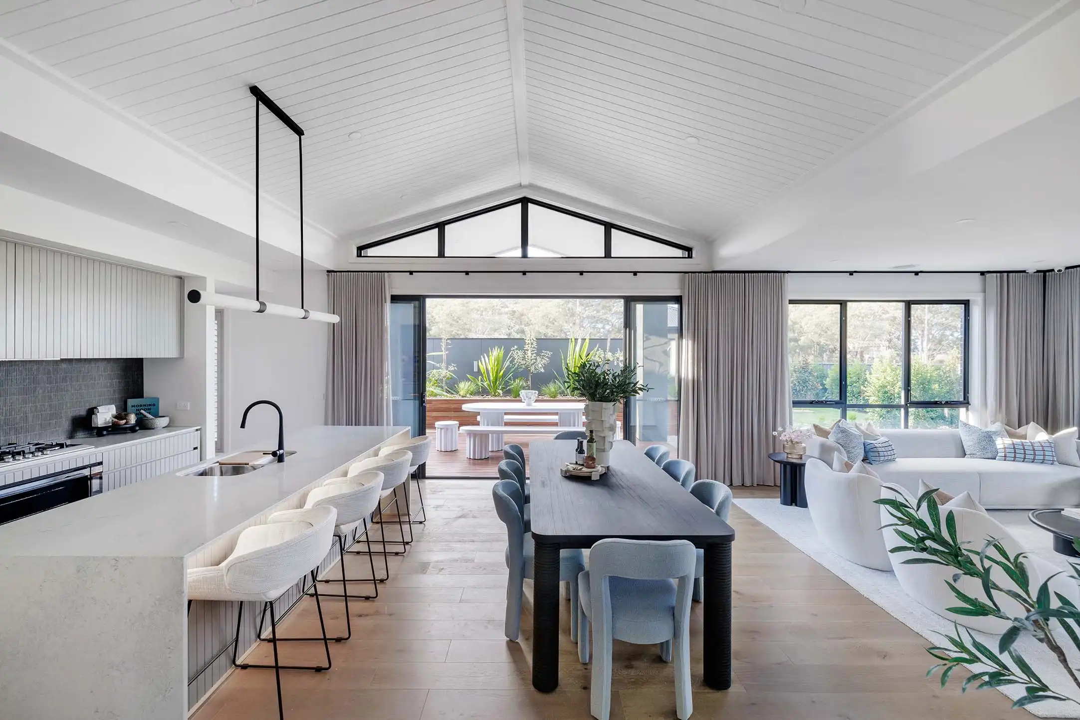 Open plan living with wood cladding on cabinetry and ceiling, blending the coastal hamptons style with timber flooring