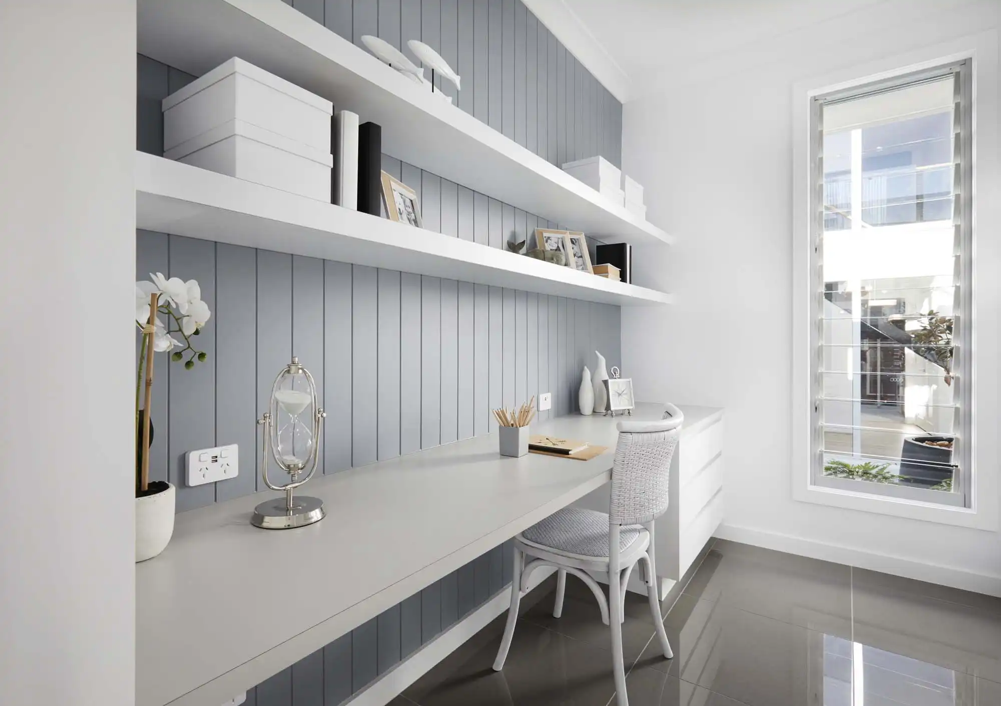 Study space with natural lighting coming through the shutters, built in shelving and cabinetry.